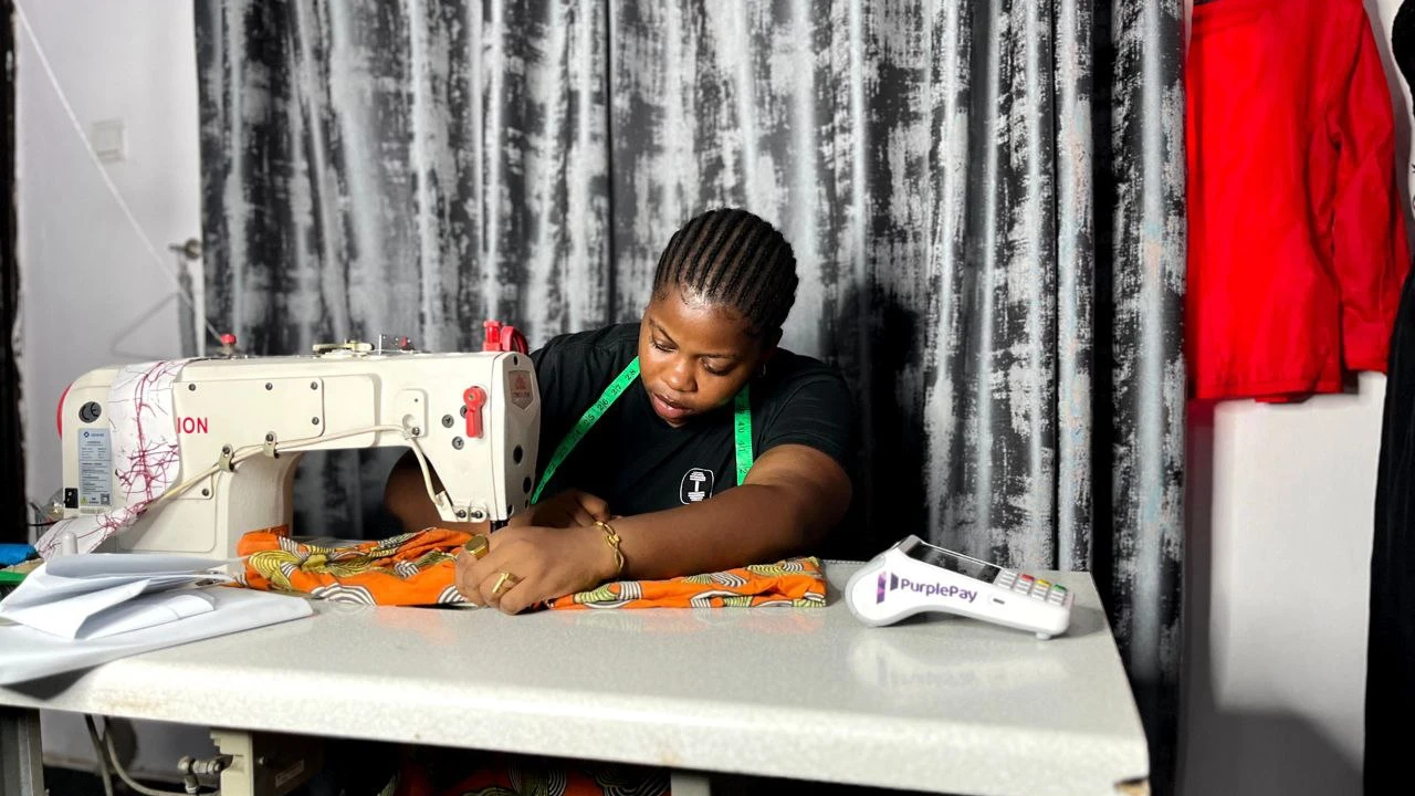 A woman using a sewing machine with the purplepay pos machine on her table